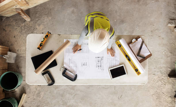 Engineering, building and aerial of construction worker with blueprint, tools and digital tablet on desk. Architect check engineering design, floorplan and drawing at workstation in construction site